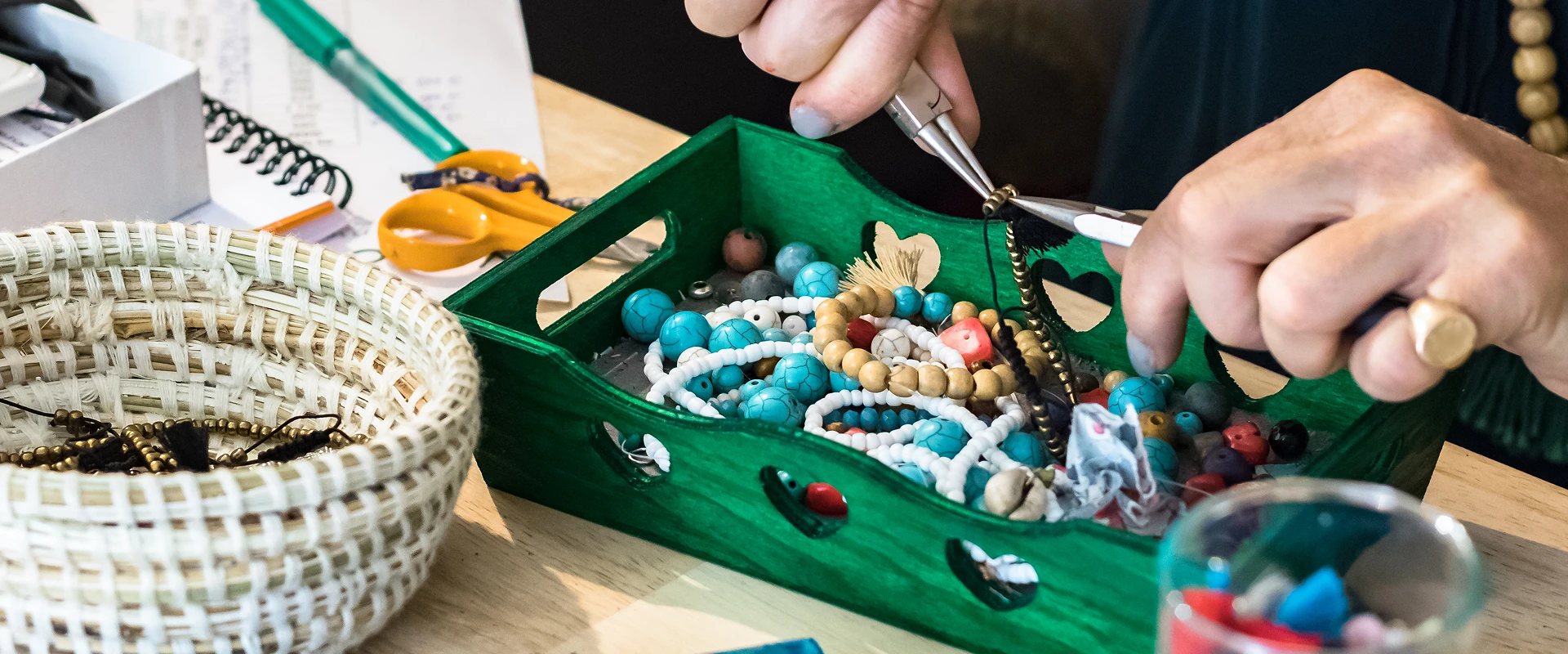 Hands crafting beaded jewelry with tools.